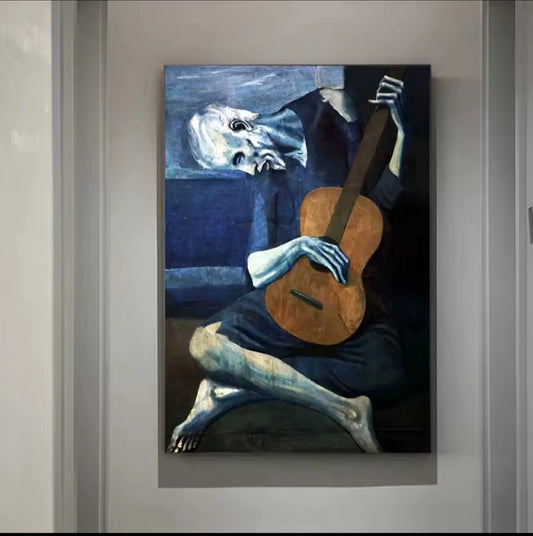 Riproduzione del celebre “Vecchio Chitarrista Cieco” di Picasso, figura malinconica blu che suona la chitarra su uno sfondo spoglio.